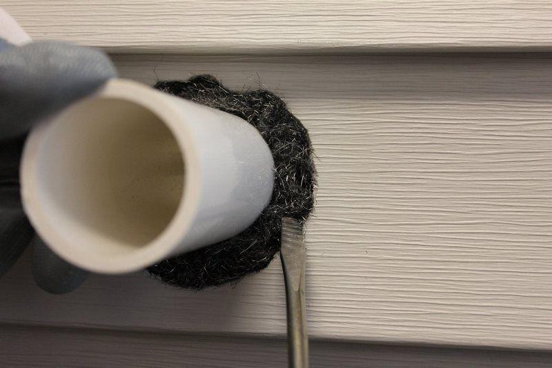 pest control technician fitting Xcluder rodent-proof stainless wire wool to a gap around a pipe